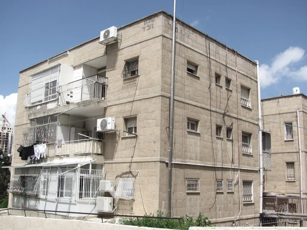 שיכון חב״ד בירושלים: בניין מצופה אבן עם סורגים, מרפסות סגורות וכביסה.