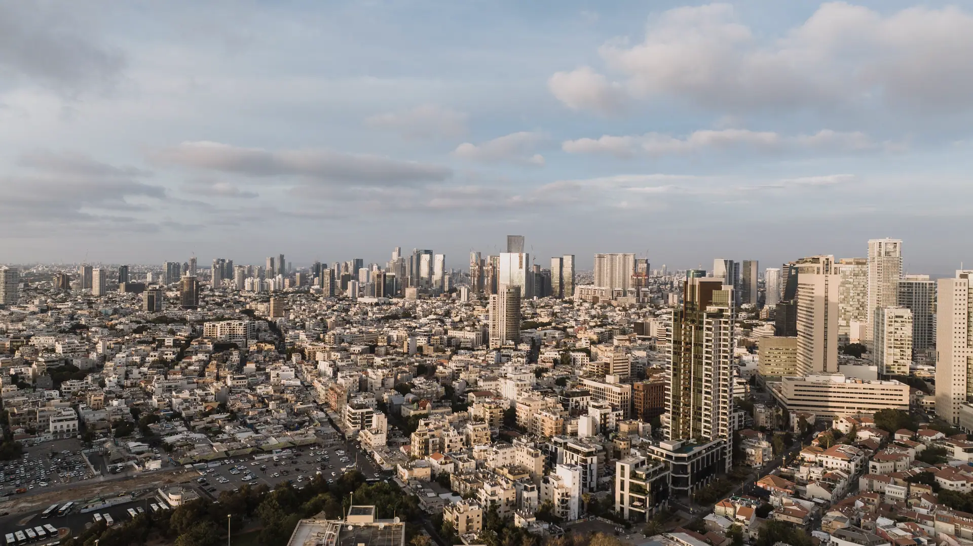 בלוקי מגורים צפופים בתל אביב ומגדלי מרכז העסקים מאחוריהם, במבט מרחפן.